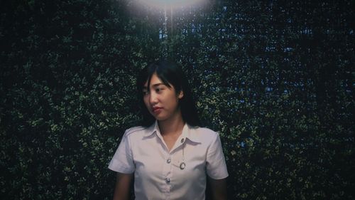 Young woman looking away while standing against hedge