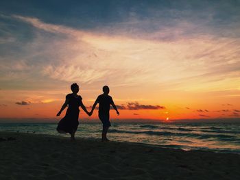 Silhouette couple walking on beach at sunset