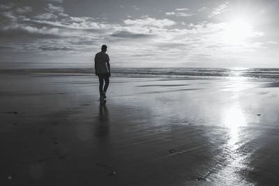 Full length rear view of man walking on beach against sky