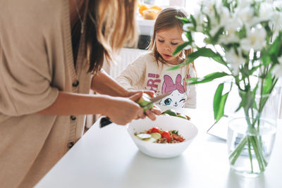 Cute little girl with long hair help to cook her mother in the kitchen at home. daughter and mom 