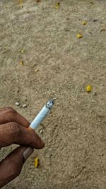 Close-up of hand holding cigarette on sand
