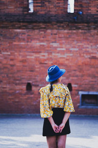 Rear view of woman in hat standing against wall