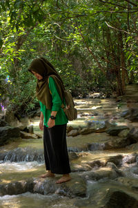 Side view of woman standing by waterfall in forest