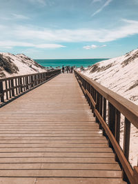 View of wooden footbridge leading towards sea against sky