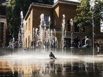 People walking on fountain against building