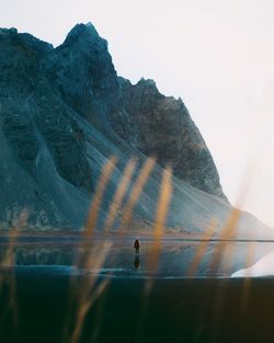 Rear view of man standing at beach against cliff