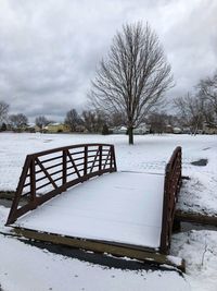 Bare trees on snow covered field against sky