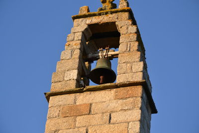 Low angle view of bell in brick wall against blue sky