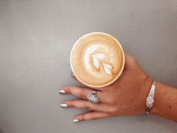 Cropped image of woman holding cappuccino on gray table