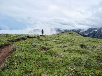 Rear view of hiker on mountain against cloudy sky