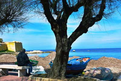 Man sitting on tree by sea against sky