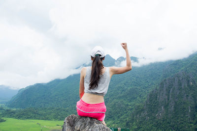 Rear view of woman sitting on mountain against sky