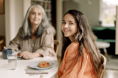 Portrait of smiling girl having breakfast with grandmother at home