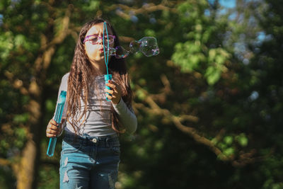 Portrait of a beautiful caucasian girl blows soap bubbles standing in the park