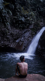 Rear view of shirtless man looking at waterfall