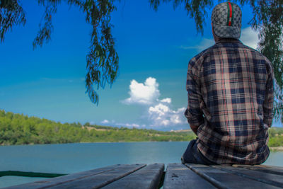 Rear view of man standing by tree against blue sky