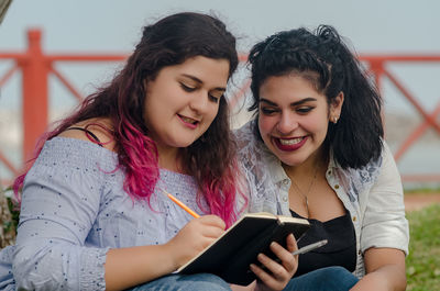 Happy friends discussing while writing in book at park