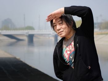 A man by the river in the sunny weather shielding his eyes from sunlight, looking at the camera.