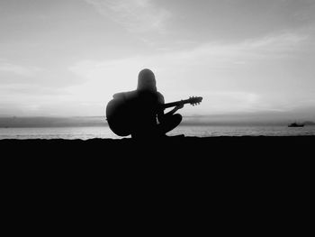 Silhouette of woman playing guitar on beach