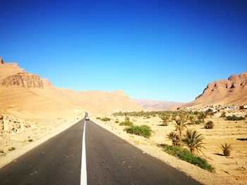 Road leading towards mountains against clear blue sky