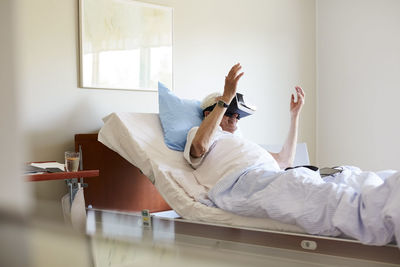 Senior man using vr glasses on bed in hospital ward