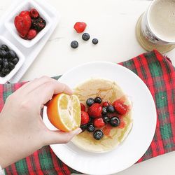 Cropped image of hand holding orange over pancakes on table