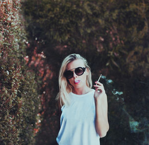 Close-up of young woman wearing sunglasses standing against trees