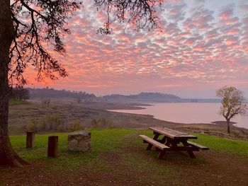 Empty bench on field against sky during sunset