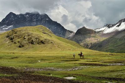 Friends with horse walking on grassy mountain during winter