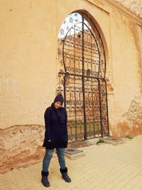 Portrait of woman standing against gate of old building