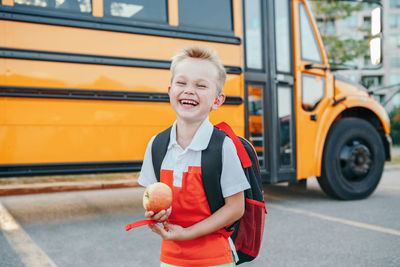 Happy laughing smiling caucasian boy student by yellow bus on first september day. back to school 