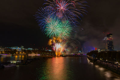 Firework display over illuminated city against sky at night