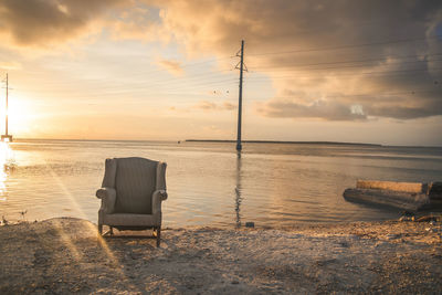 Abandoned chair at beach during sunset