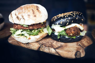 Delicious white and black burgers with green lettuce and cheese served on wooden board on black table