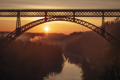 Silhouette bridge over river against sky during sunset