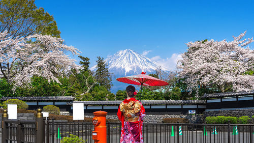 Rear view of woman with arms outstretched standing against clear blue sky