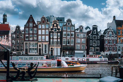 Boats on canal by buildings against cloudy sky in city