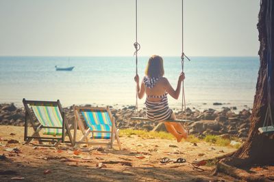 Rear view of woman swinging on swing at beach against sky