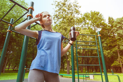 Low angle view of young woman standing on railing against clear sky