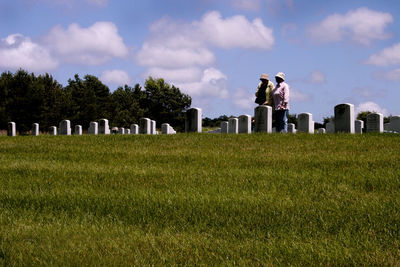 Women standing by gravestones at cemetery against cloudy sky