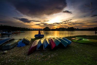 Boats moored on lake against sky at sunset