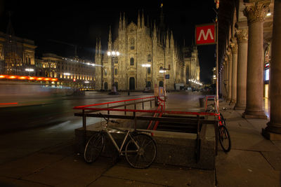 Bicycles on road by illuminated buildings at night