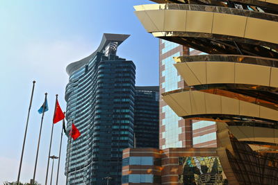 Low angle view of flags by modern buildings in city against clear sky