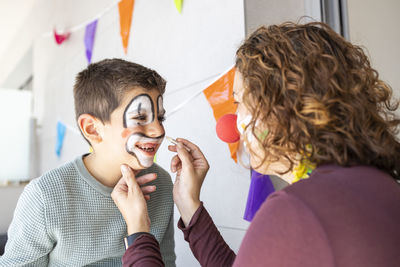 Mother painting her son's face like a clown