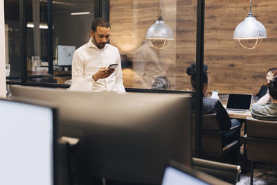 Businessman using smart phone standing at illuminated creative office