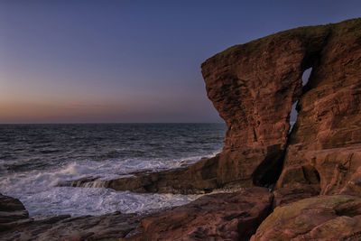 Rock formation on beach against sky during sunset