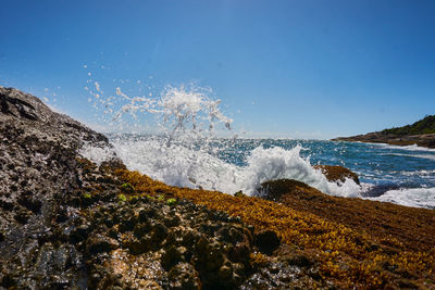 Sea waves splashing on rocks against clear sky