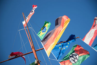 Low angle view of flags against clear blue sky