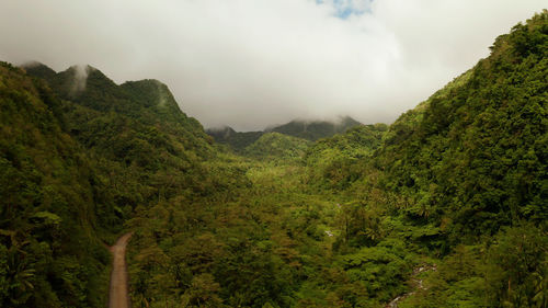 Mountains covered rainforest, trees and river in cloudy weather, aerial drone. camiguin, philippines
