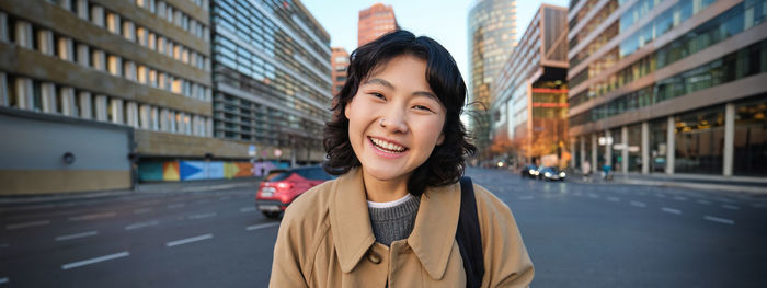 Portrait of young woman standing against buildings